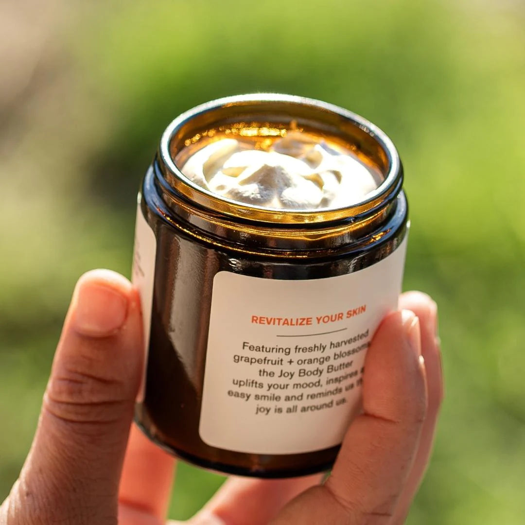 A person holding a jar of body butter with a green background.