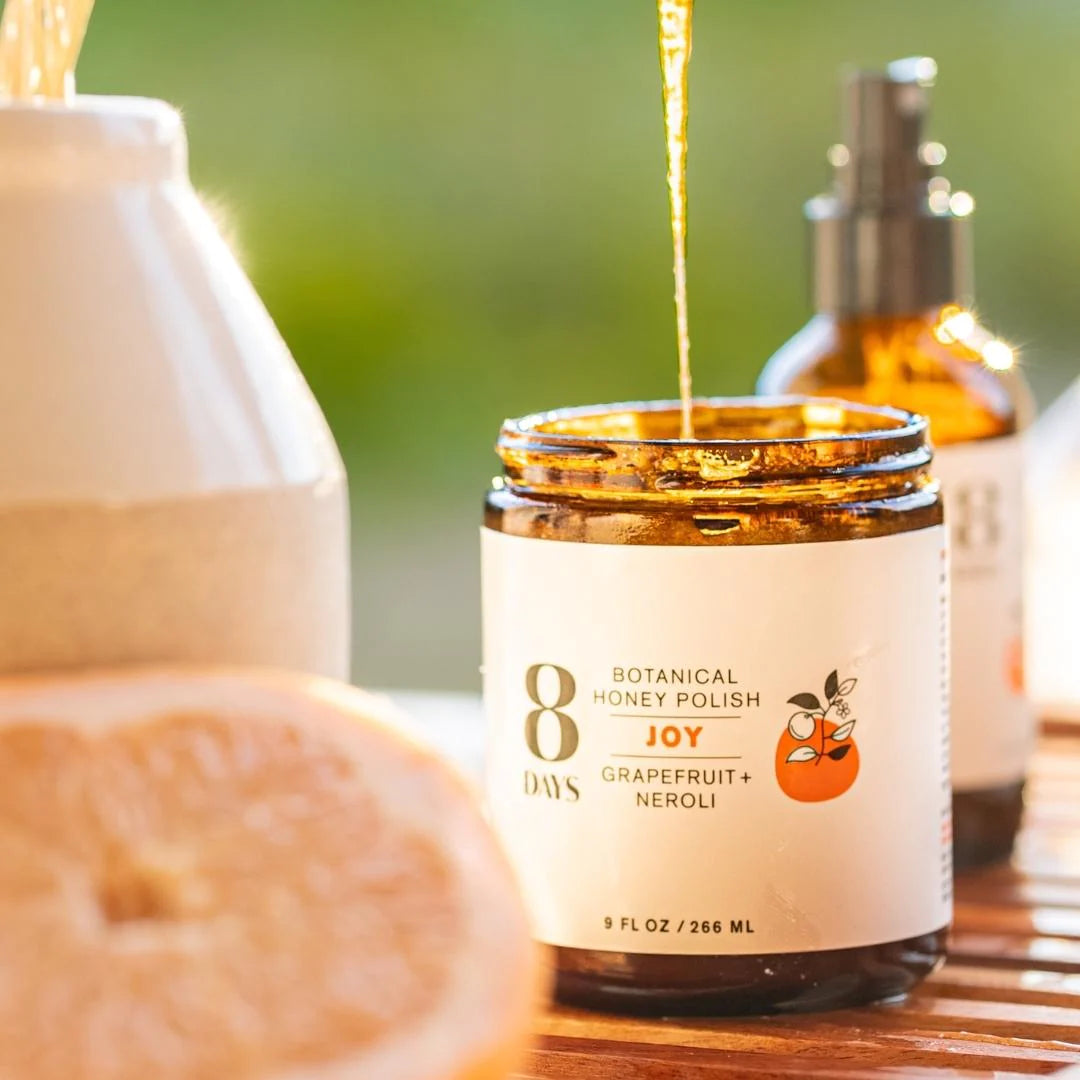 A jar of 8 Days Botanicals Organic Body Polish - Joy sitting on a table with a grapefruit.