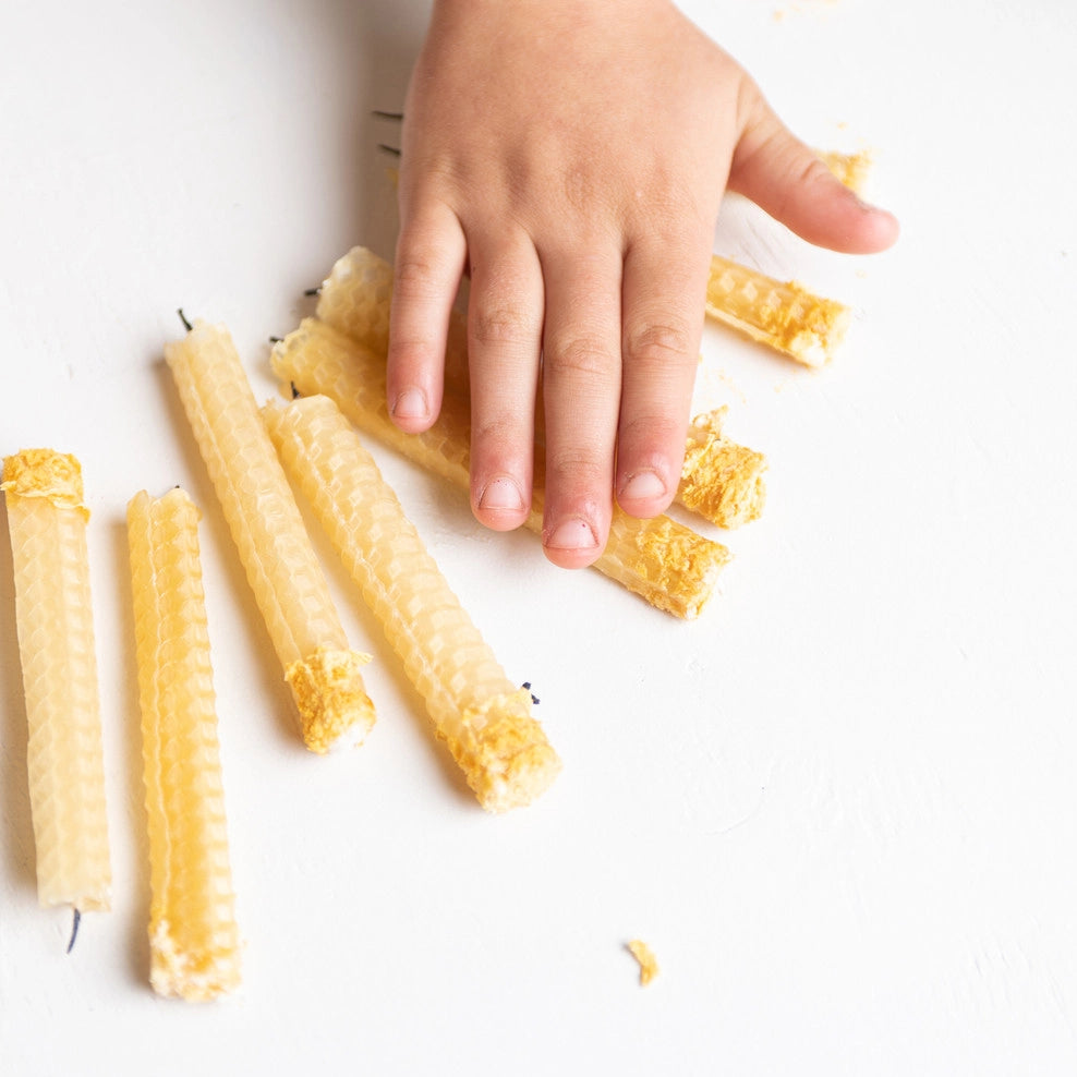 A child hand over a collection of Beeswax Candle Kit candles.