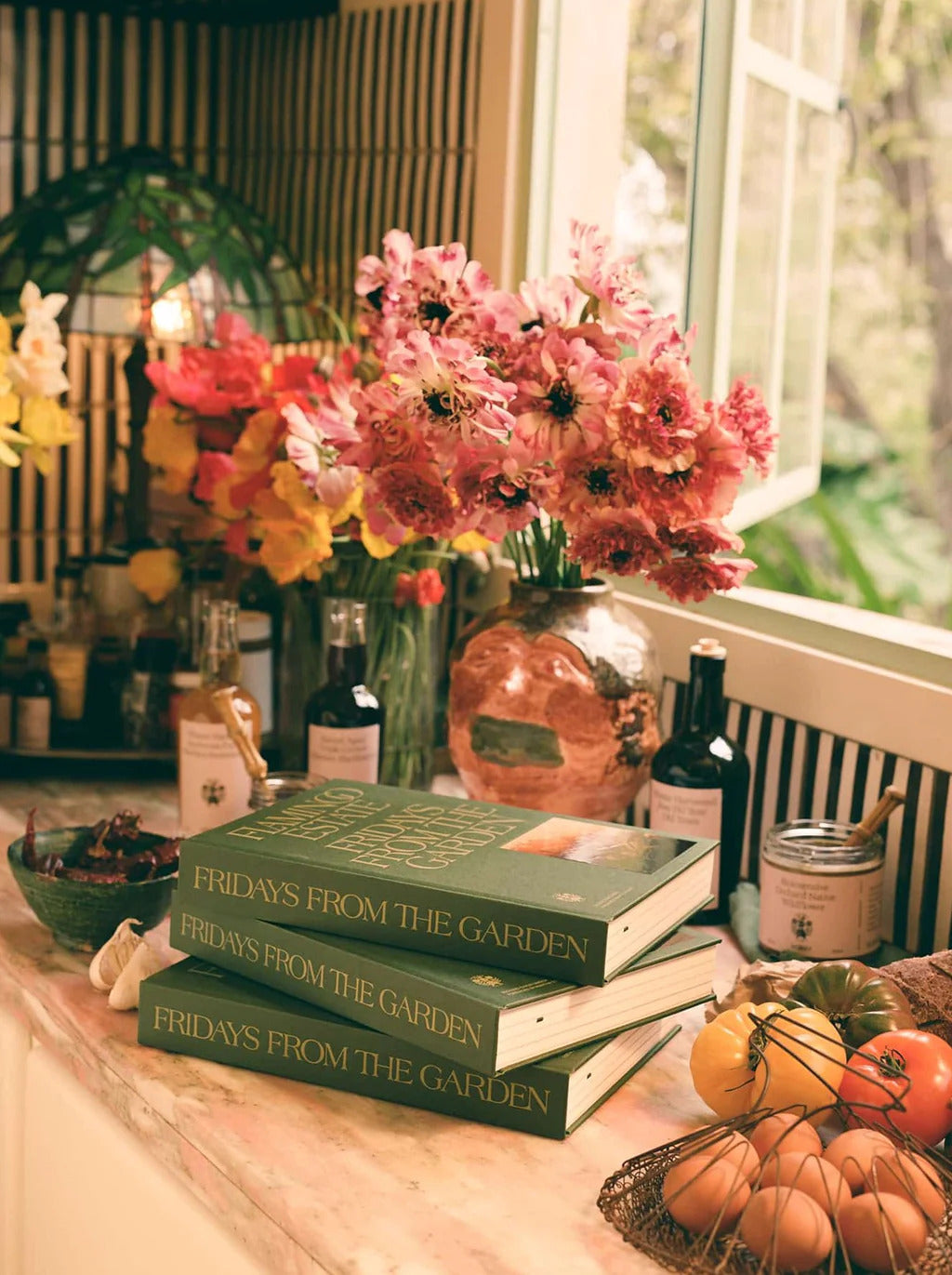 Flamingo Estate Fridays From the Garden Cookbook resting on a kitchen counter surrounded by different bottles of olive oil.