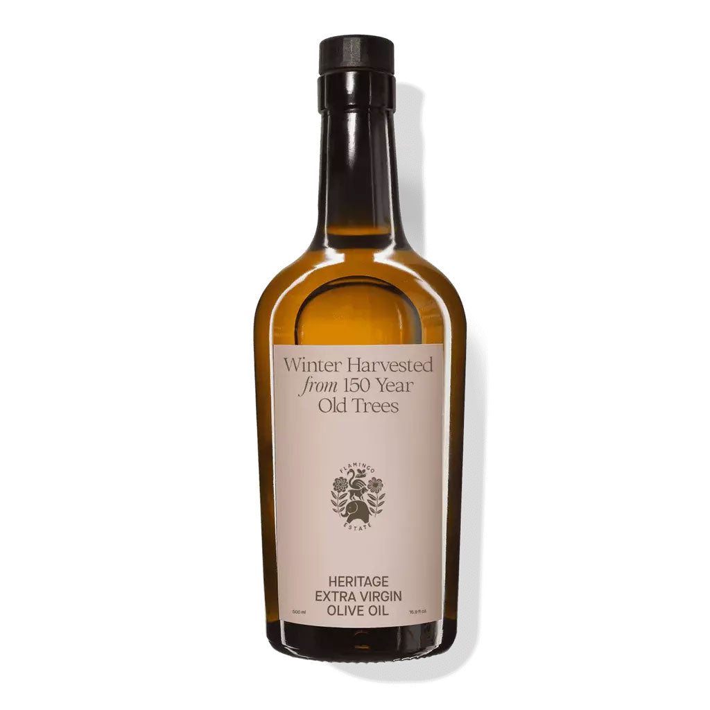 A glass bottle of Flamingo Estate Heritage Extra Virgin Cold Pressed Olive Oil. The label has the Flamingo Estate logo as well as the words "winter harvested from 150 year old trees. heritage extra virgin olive oil".