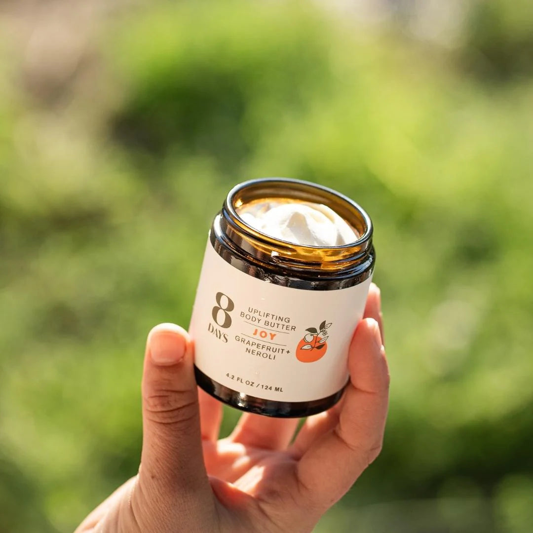 A hand holding a jar of 8 Days Botanicals Organic Body Butter "Joy".